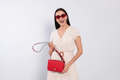 Photo of Beautiful young woman with red bag in stylish sunglasses on light grey background