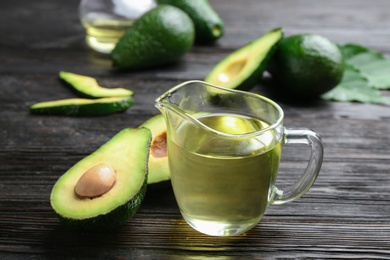 Photo of Jug of natural oil and avocados on dark wooden background