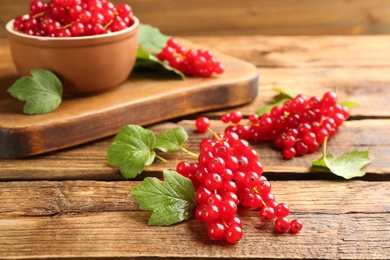 Photo of Delicious red currants and leaves on wooden table