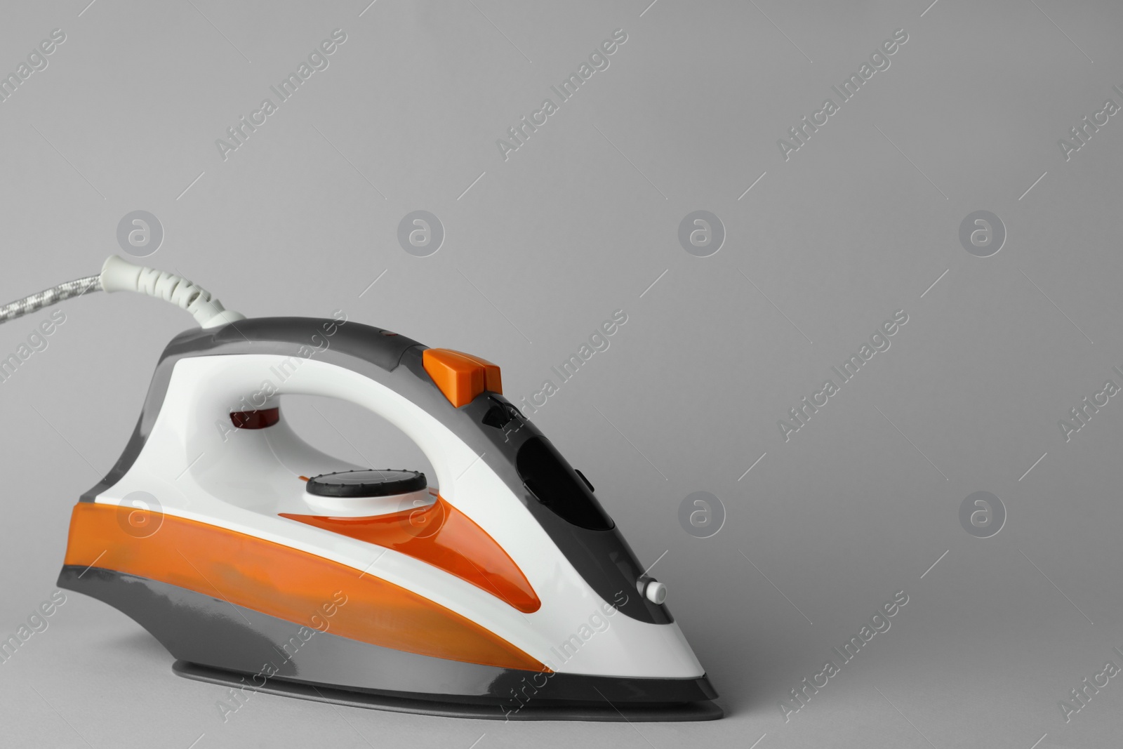 Photo of One modern iron on light grey background, space for text. Home appliance