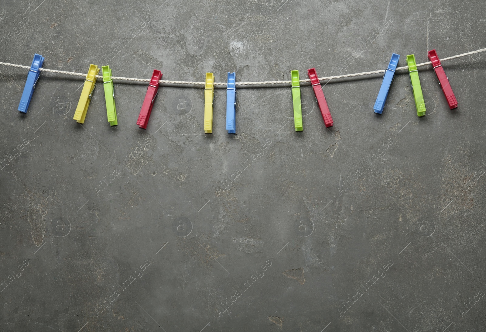 Photo of Colorful plastic clothespins and rope on grey stone background. Space for text