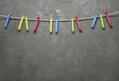 Photo of Colorful plastic clothespins and rope on grey stone background. Space for text