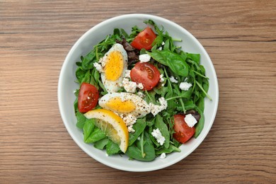 Delicious salad with boiled egg, tomatoes and cheese in bowl on wooden table, top view