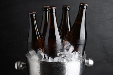 Photo of Metal bucket with beer and ice cubes on black background, closeup