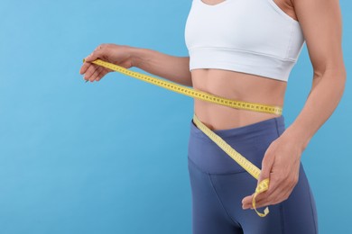 Photo of Slim woman measuring waist with tape on light blue background, closeup and space for text. Weight loss