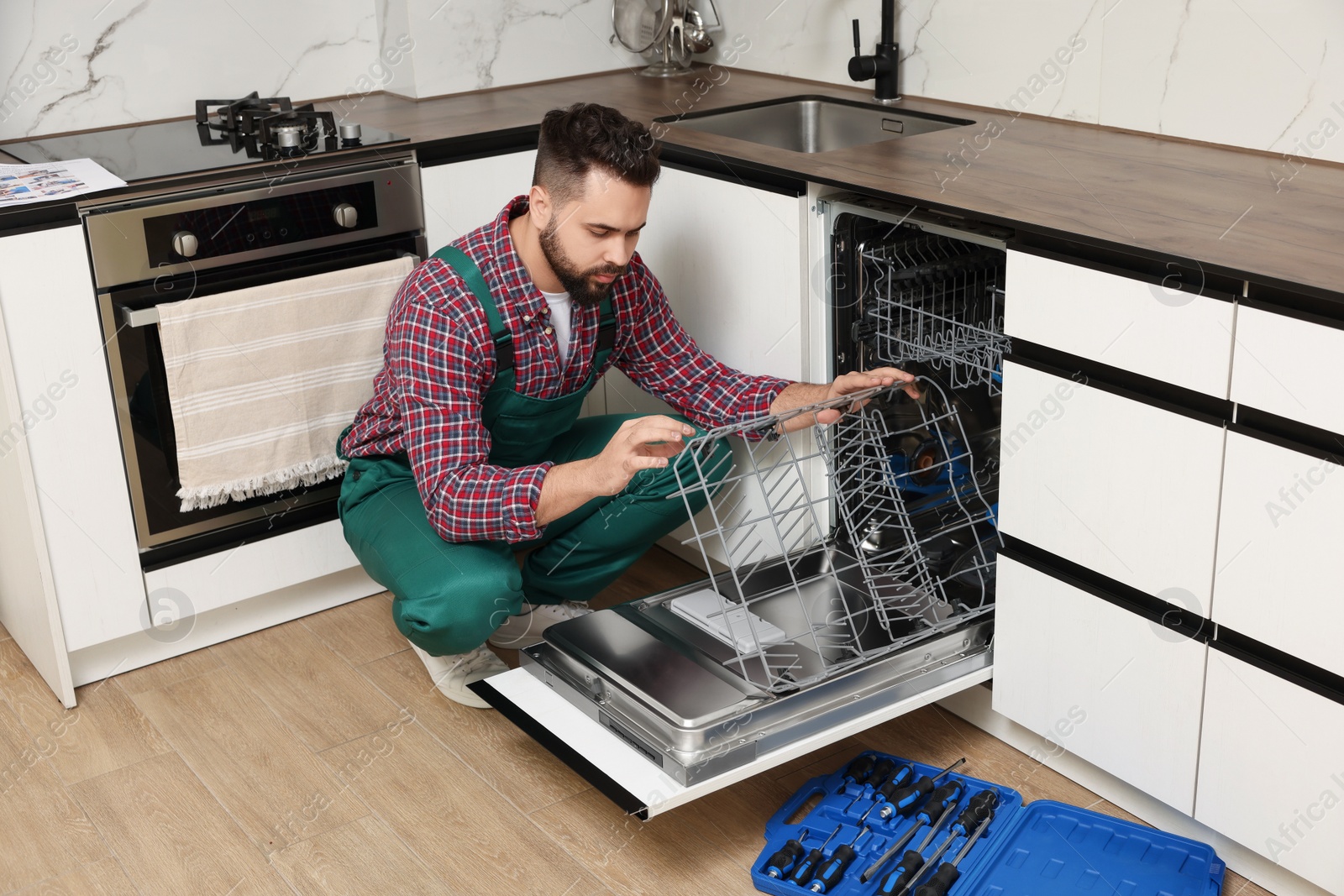 Photo of Serviceman examining dishwasher lower rack in kitchen