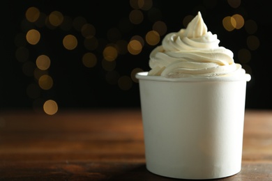 Cup of tasty frozen yogurt on wooden table against blurred lights. Space for text