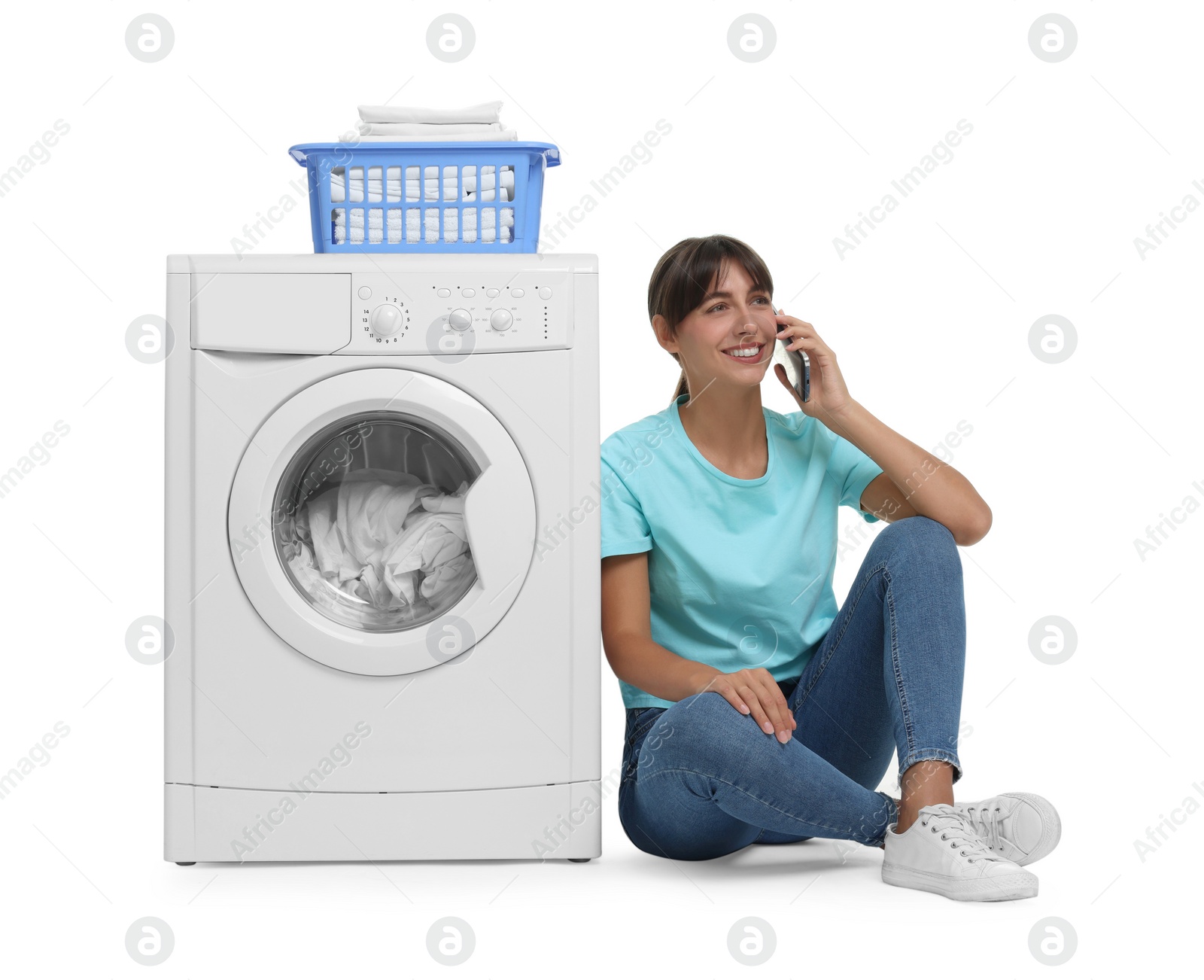 Photo of Beautiful woman talking on smartphone near washing machine with laundry against white background