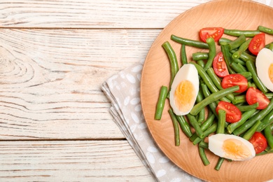 Photo of Plate with tasty green beans, eggs and  tomatoes on wooden table, top view