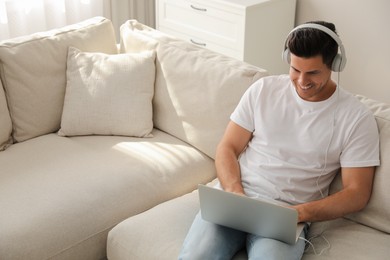 Photo of Man with laptop and headphones sitting on sofa at home