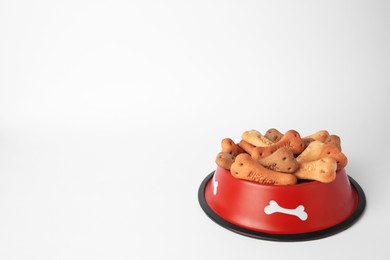 Bone shaped dog cookies in feeding bowl on white background, space for text