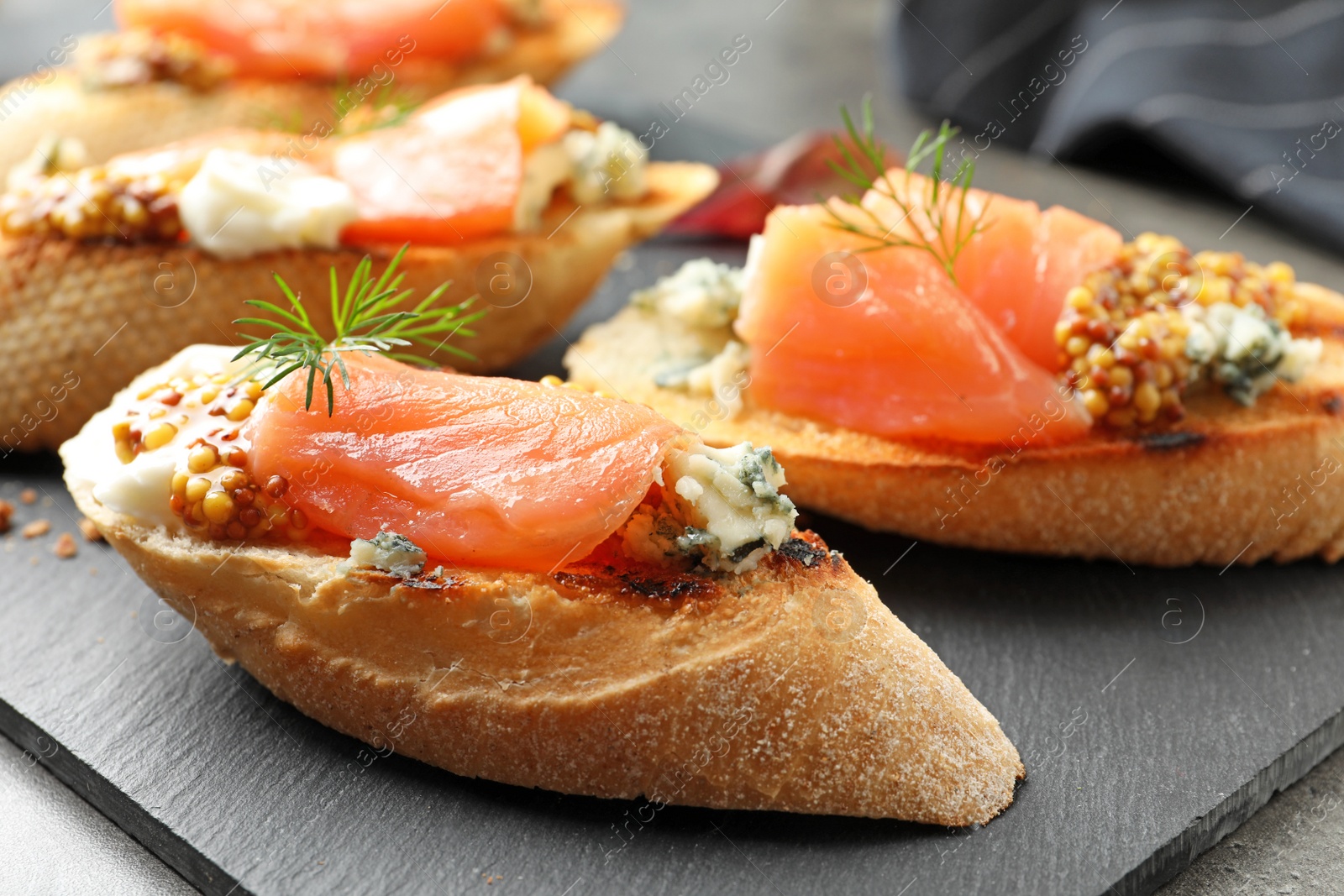 Photo of Tasty bruschettas with salmon and blue cheese on slate plate, closeup