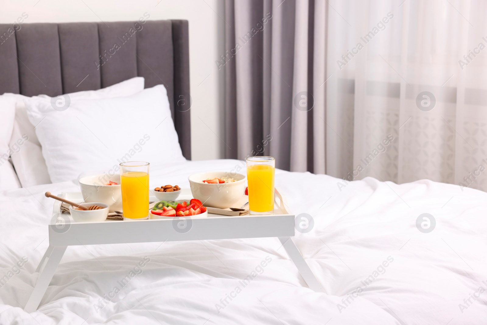 Tasty breakfast served in bed. Oatmeal, juice, fruits, almonds and honey on tray, space for text Photo of Tasty breakfast served in bed. Oatmeal, juice, fruits, almonds and honey on tray, space for text