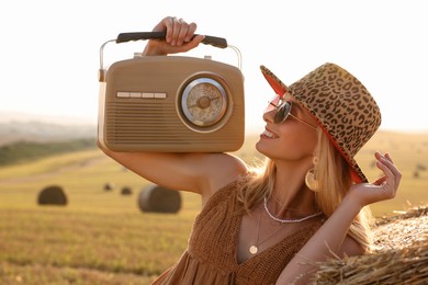 Happy hippie woman with receiver near hay bale in field