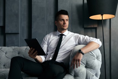 Photo of Handsome businessman with tablet on sofa indoors. Luxury lifestyle