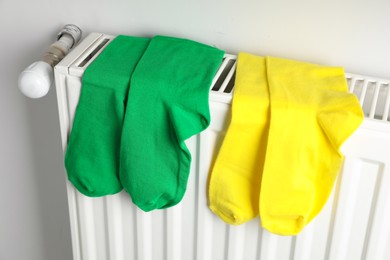 Different colorful socks on heating radiator near white wall