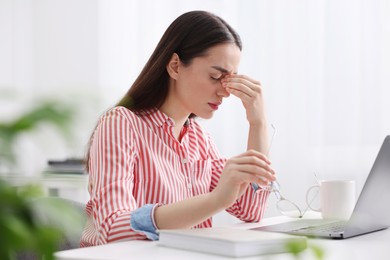 Photo of Woman with glasses suffering from headache at workplace in office