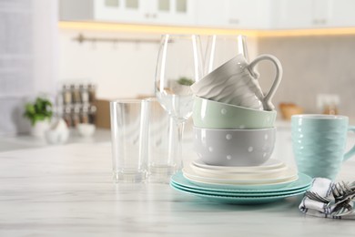 Many different clean dishware, cutlery, glasses and cups on white marble table in kitchen. Space for text