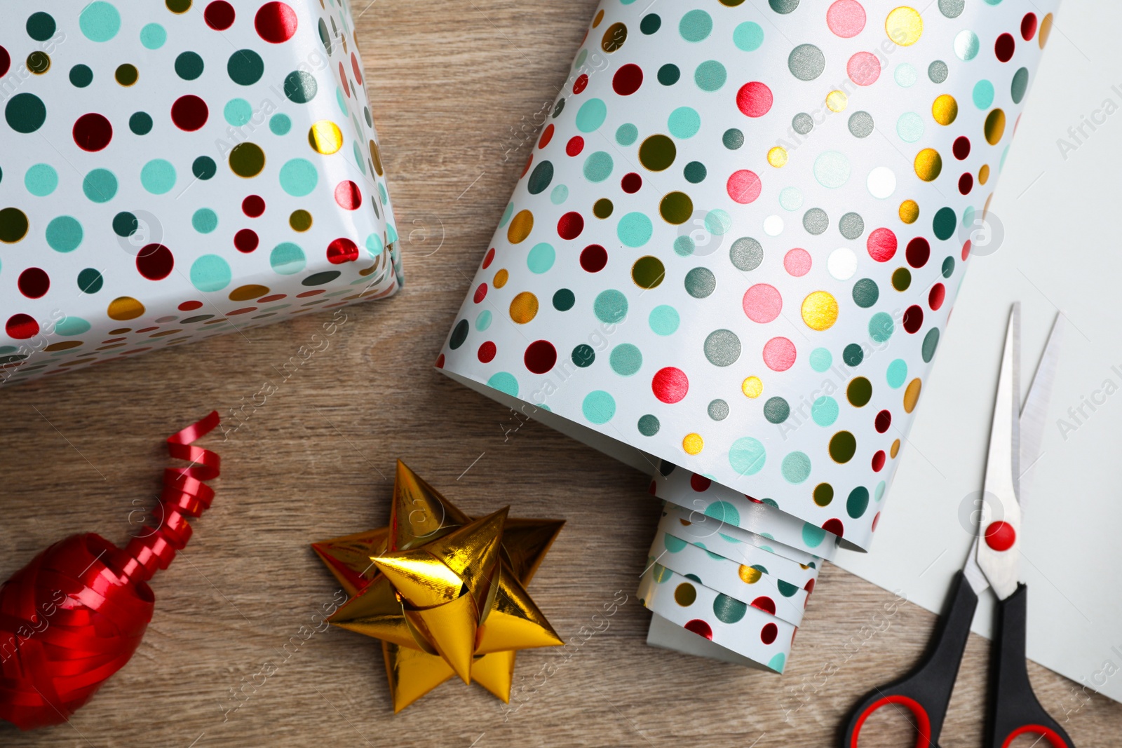 Photo of Roll of wrapping paper, scissors, gift bow and box on wooden table, flat lay