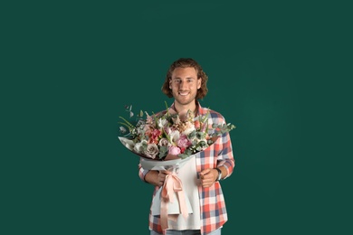 Young handsome man with beautiful flower bouquet on green background