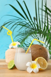 Photo of Composition with glass of coconut water on wooden table against blue background