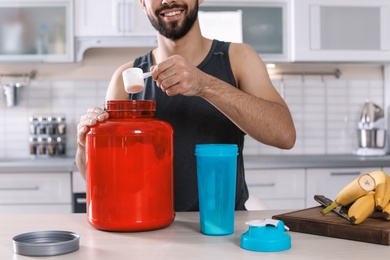 Young man preparing protein shake at table in kitchen, closeup