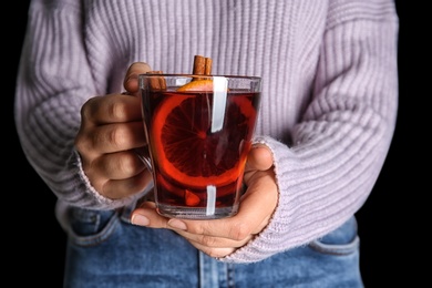 Woman holding cup with hot mulled wine against dark background, closeup