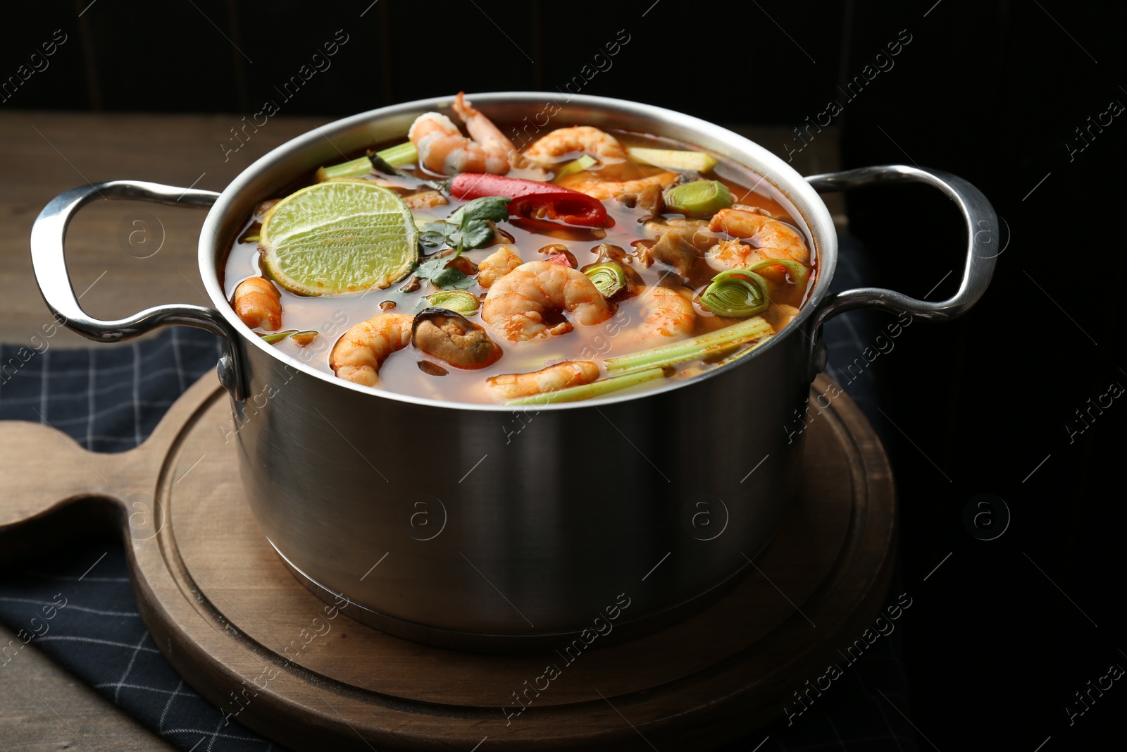 Photo of Saucepan with delicious Tom Yum soup on wooden table