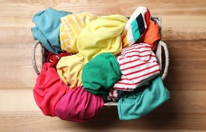 Wicker basket with laundry on wooden surface, top view