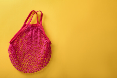 Photo of Empty pink net bag on yellow background, top view. Space for text