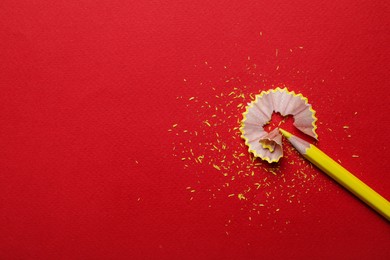 Photo of Yellow pencil and wooden shaving on red background, flat lay. Space for text