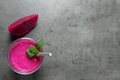 Photo of Glass of tasty pitahaya smoothie, fruit and fresh mint on grey table, flat lay. Space for text
