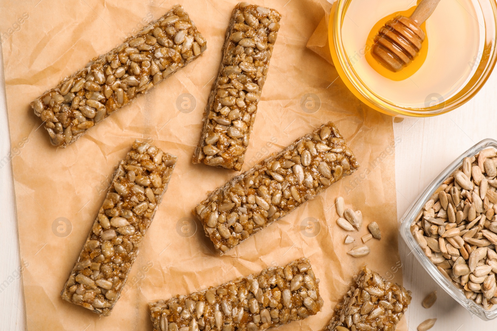 Photo of Delicious sweet kozinaki bars, honey and sunflower seeds on white wooden table, flat lay