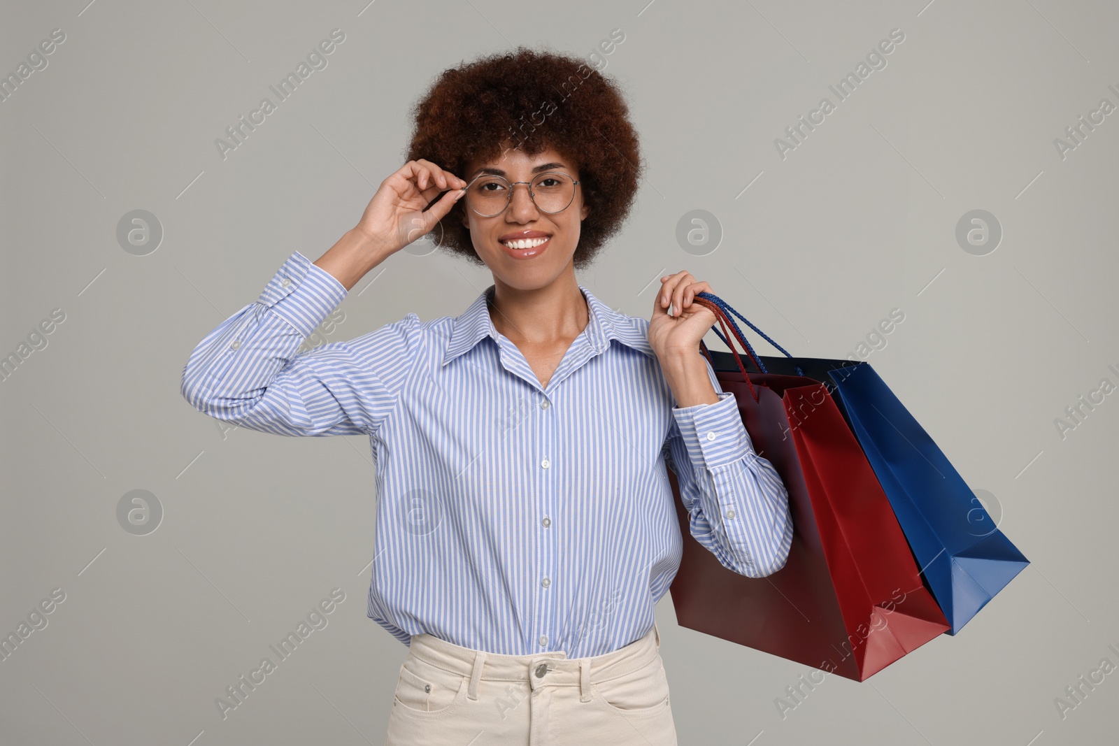 Photo of Happy young woman in stylish eyeglasses with shopping bags on grey background