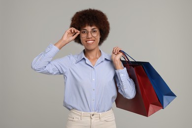 Happy young woman in stylish eyeglasses with shopping bags on grey background