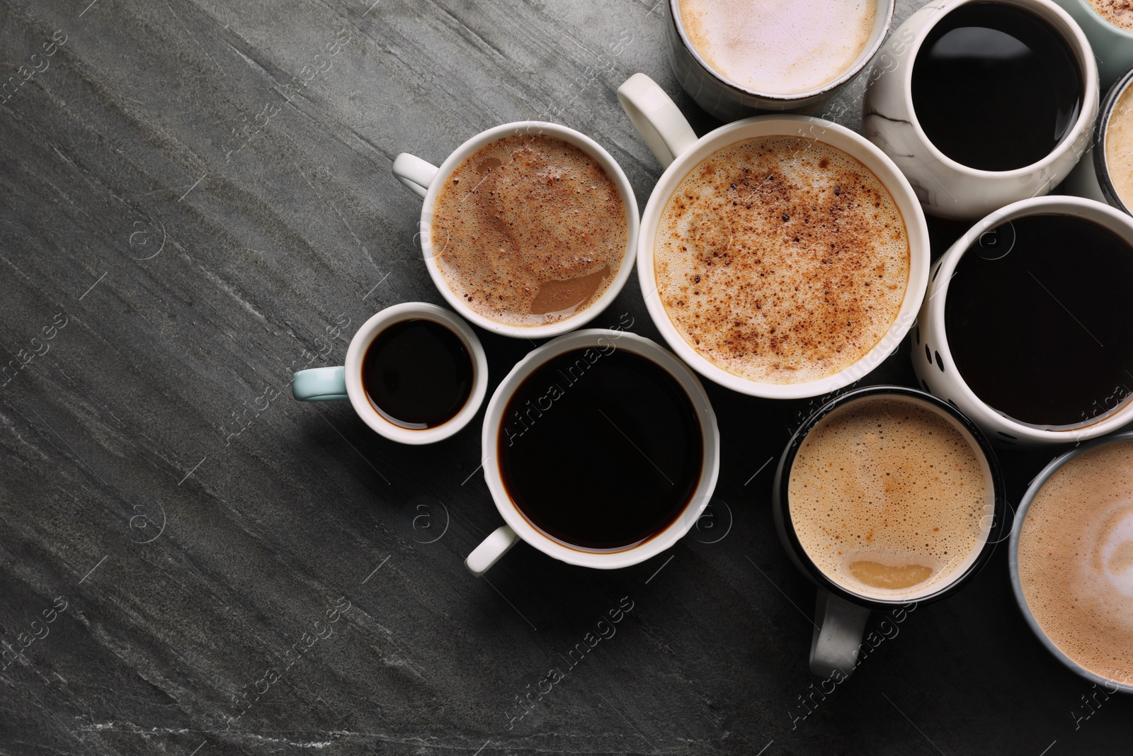 Photo of Many cups of different coffees on slate table, flat lay. Space for text