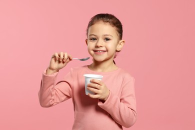 Girl with tasty yogurt on pink background