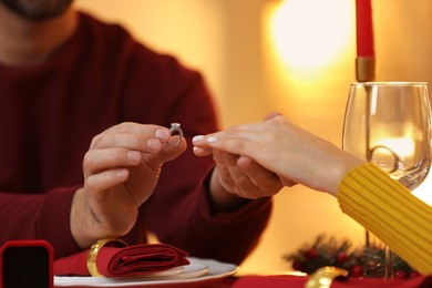Photo of Making proposal. Man putting engagement ring on his girlfriend's finger at home on Christmas, closeup