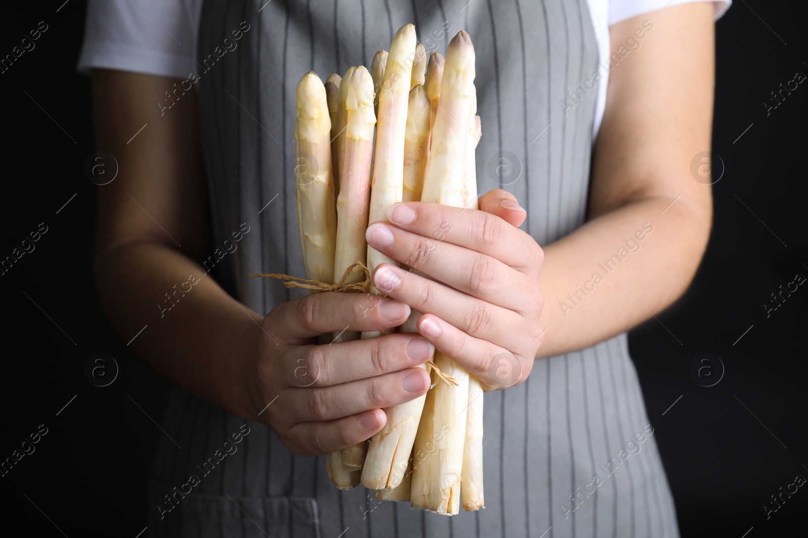 Photo of Woman holding fresh white asparagus on black background, closeup