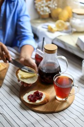 Photo of Woman spreading butter onto bread at table indoors, focus on aromatic tea