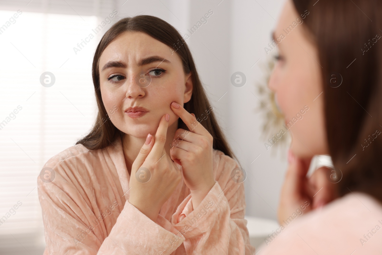 Photo of Young woman with skin problem looking at mirror indoors