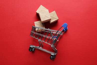 Photo of Small metal shopping cart with cardboard boxes on red background, top view