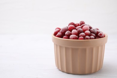 Photo of Frozen red cranberries in bowl on white table, closeup. Space for text