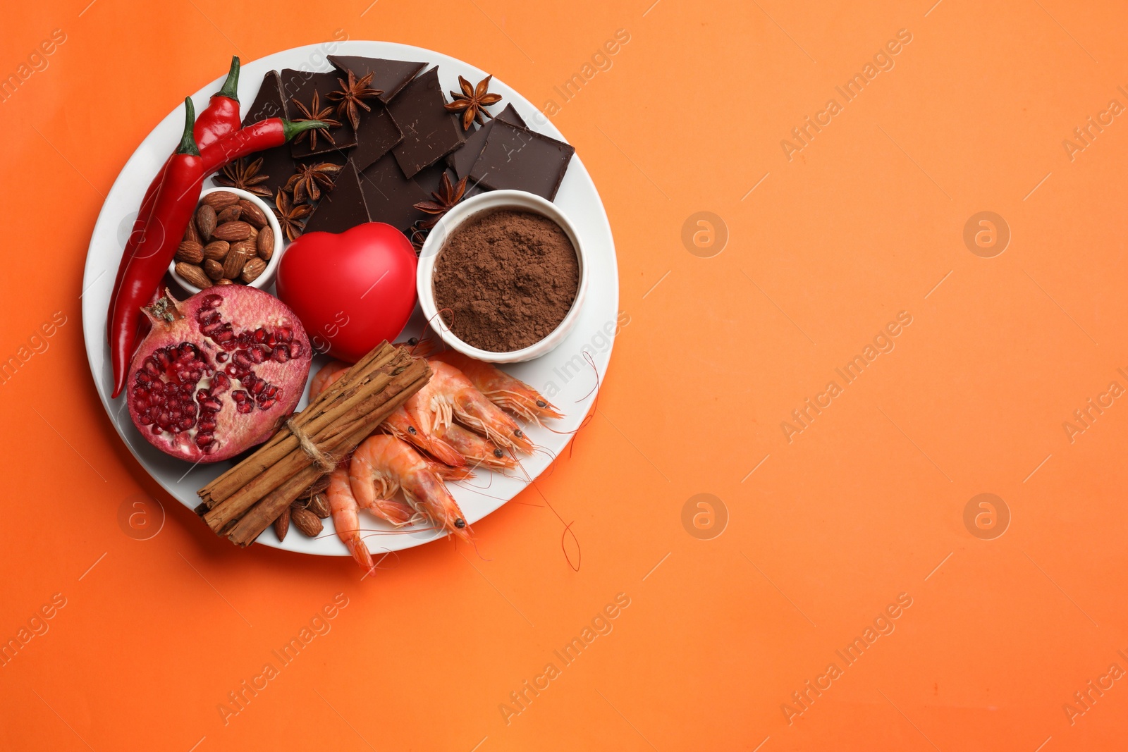 Photo of Natural aphrodisiac. Different products and heart model on orange background, top view. Space for text