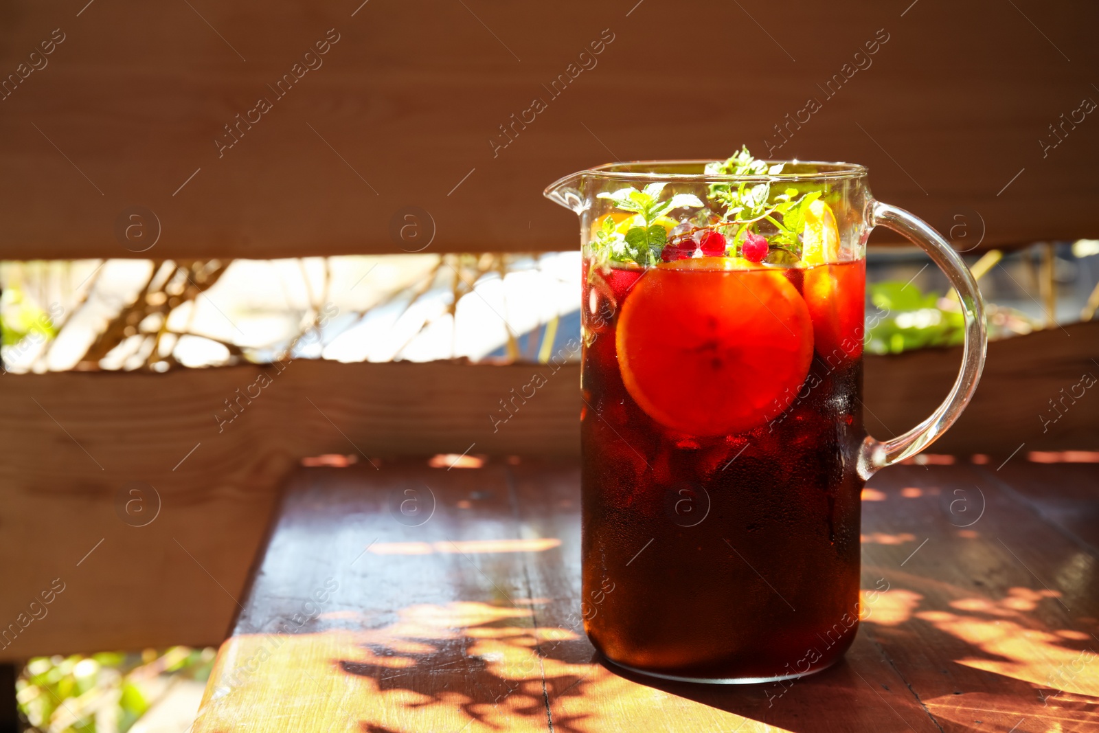 Photo of Jug with delicious refreshing cocktail on table against blurred background