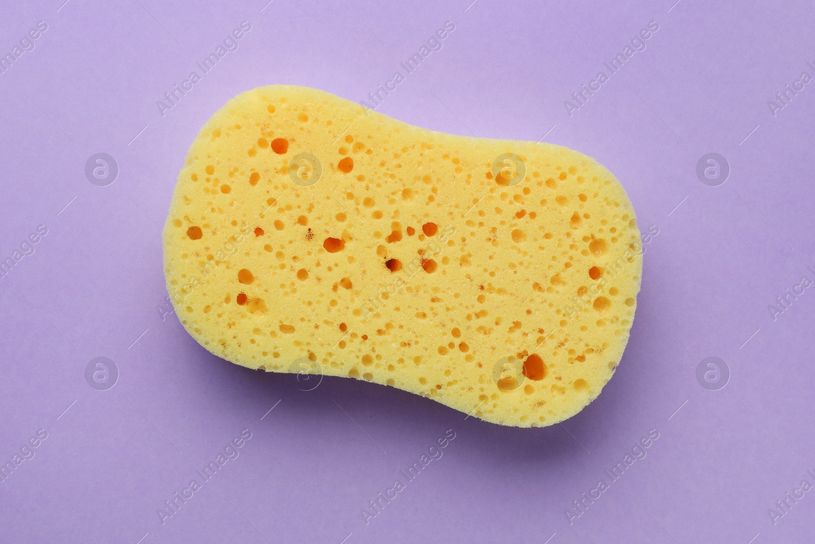 Photo of New yellow sponge on violet background, top view
