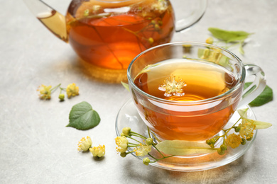 Photo of Cup of tea and linden blossom on light grey table. Space for text