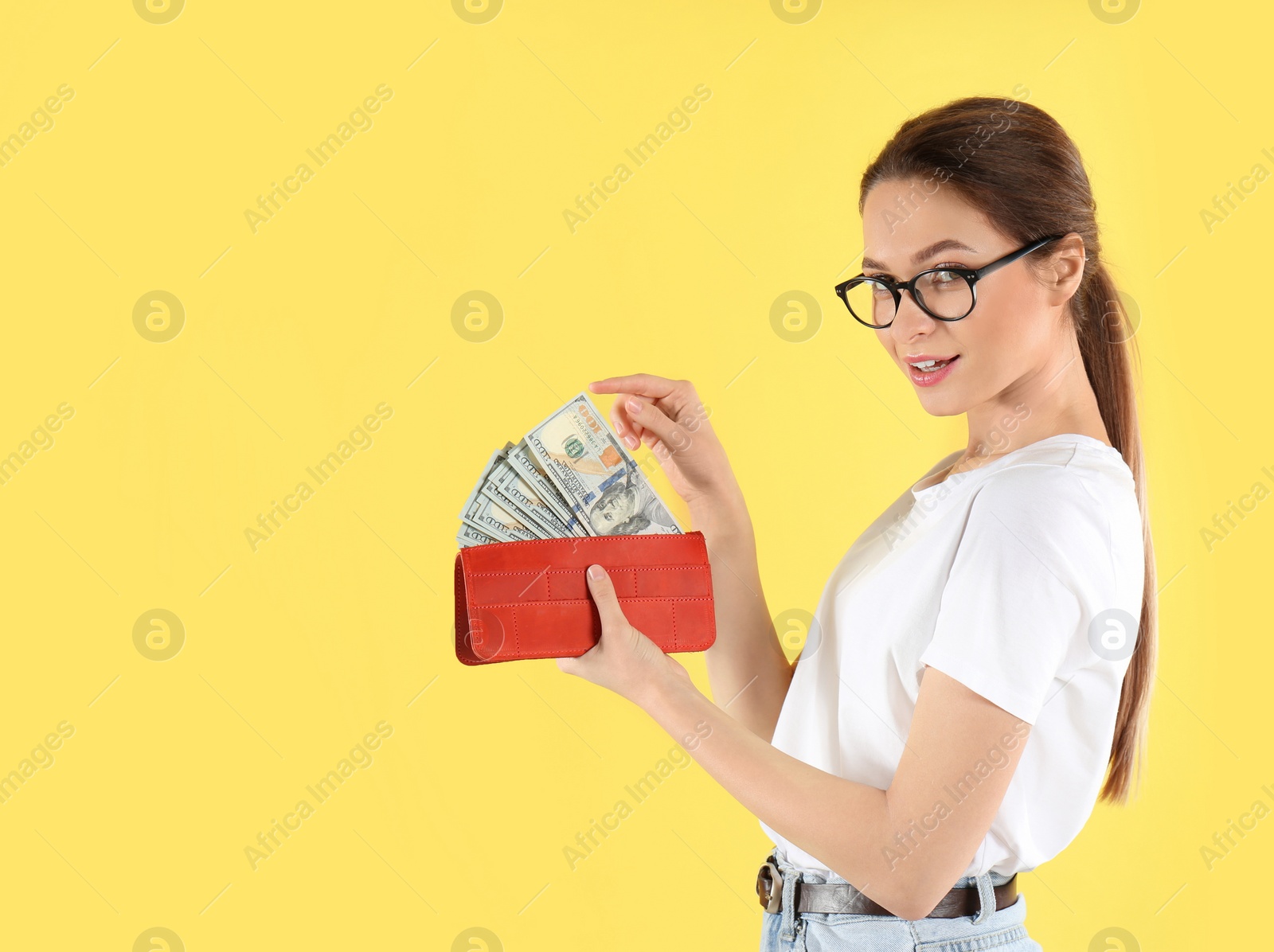 Photo of Young woman with wallet full of money on yellow background