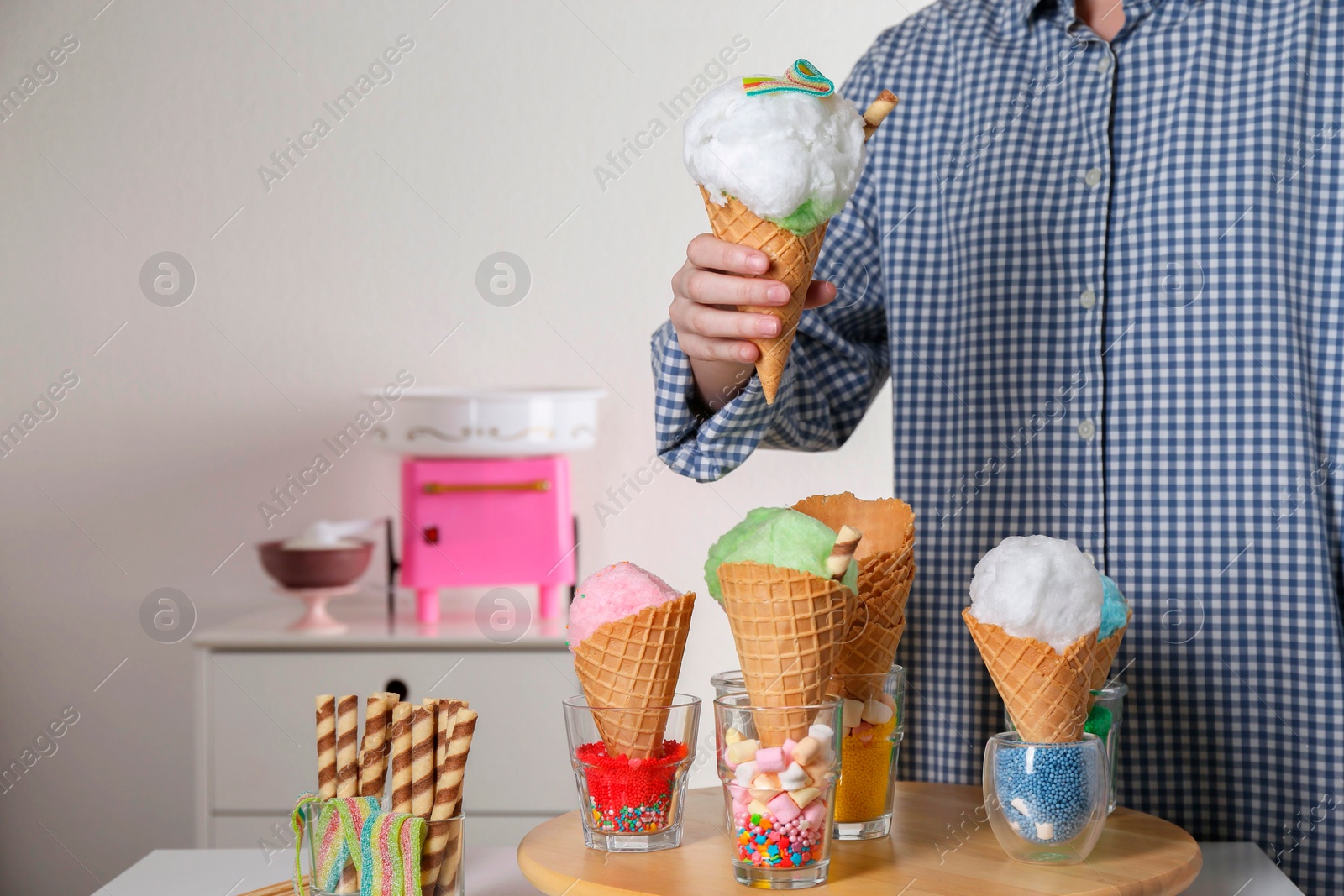 Photo of Woman holding waffle cone with cotton candy indoors, closeup