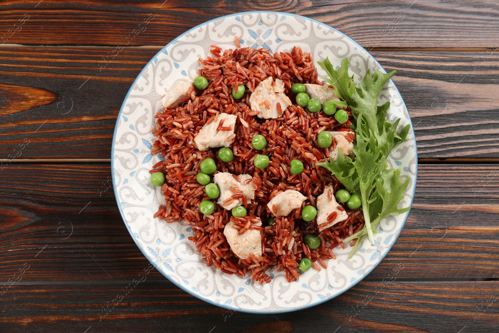 Photo of Tasty brown rice with meat and vegetables on wooden table, top view